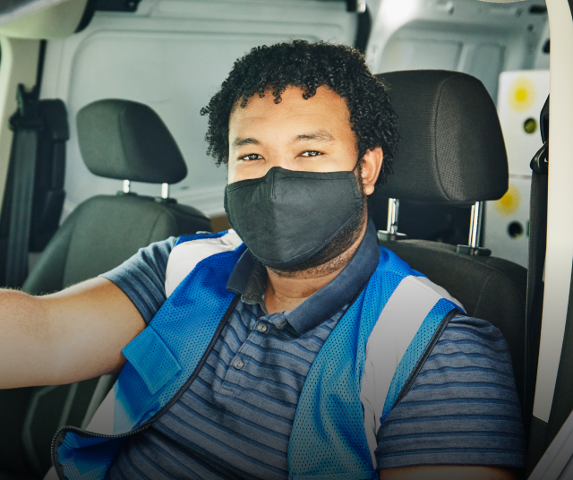 A man in a mask, sitting in the drivers seat of a van.